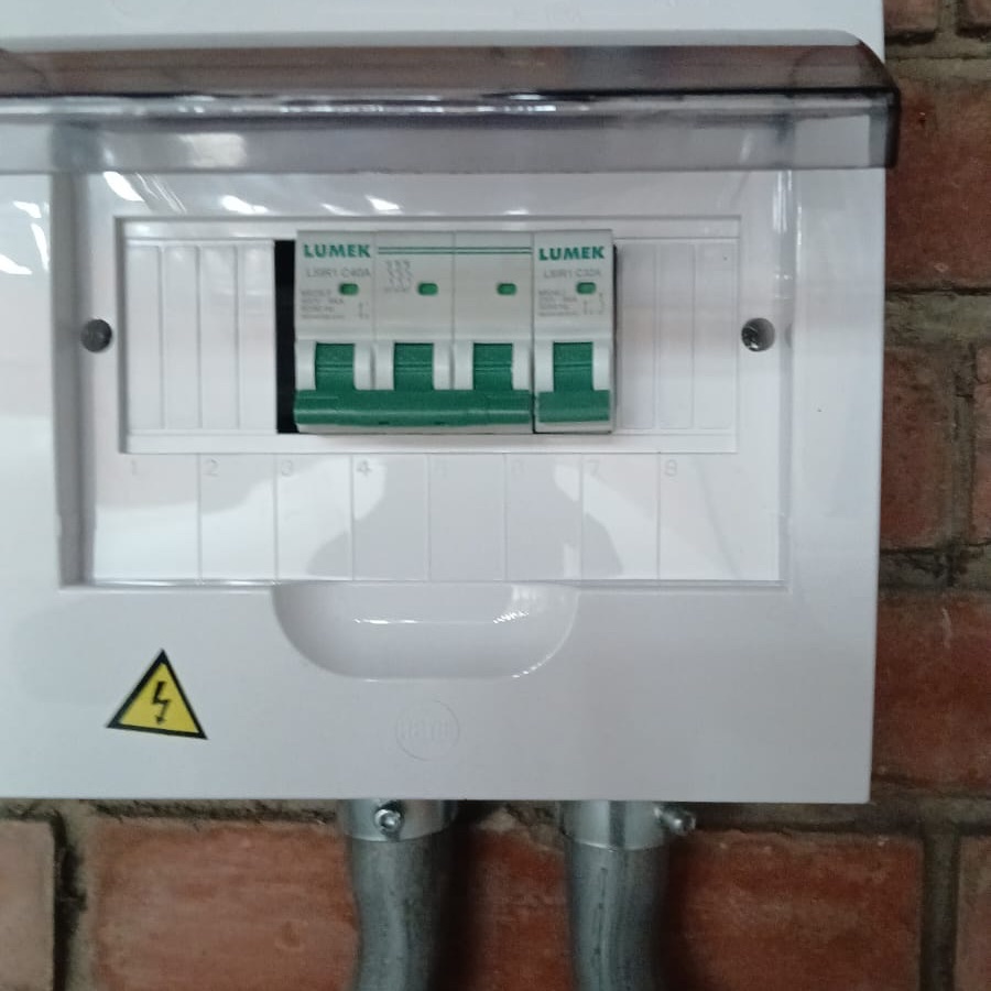 Tablero eléctrico con breakers sobre pared de ladrillo y tubería metálica